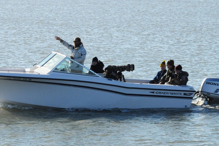 Five people in a speedboat with cameras on a lake.